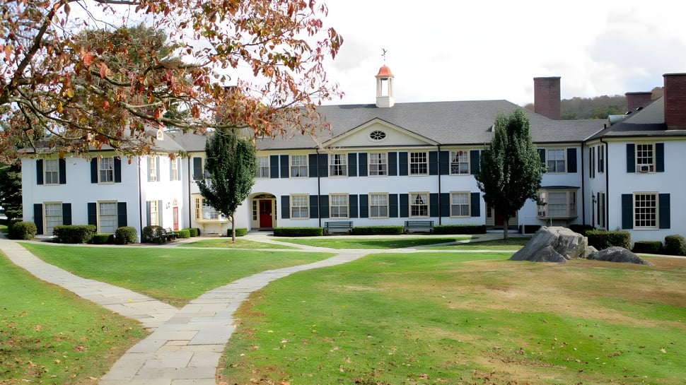 Das weiße kolonialstil Gebäude mit rotem Dach der The Frederick Gunn School steht auf einem gepflegten Rasen umgeben von herbstlichen Bäumen.