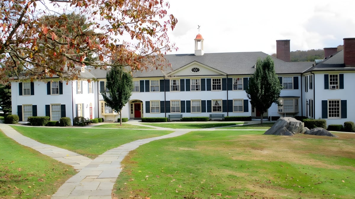 Das weiße kolonialstil Gebäude mit rotem Dach der The Frederick Gunn School steht auf einem gepflegten Rasen umgeben von herbstlichen Bäumen.