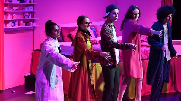 Eine Gruppe von Schülern der The Friends’ School trägt farbenfrohe Roben in einem Raum mit pink-lila Beleuchtung.