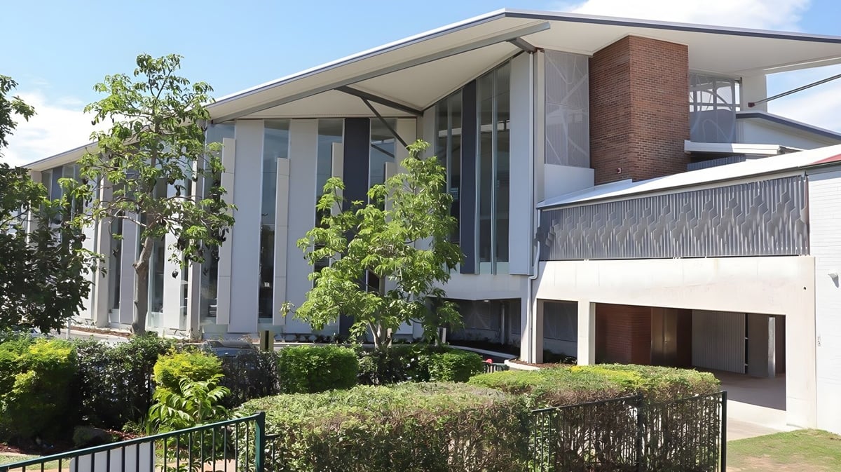 Das moderne mehrstöckige Gebäude mit großen Fenstern und Balkon auf dem Campus der The Gap State High School ist von üppigem Grün umgeben.