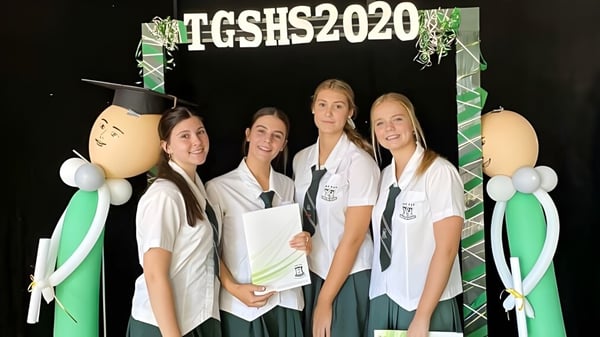 Eine Gruppe von vier Schülerinnen steht vor einem Hintergrund mit dem Schriftzug TGSHS2020 auf dem Campus der The Gap State High School.