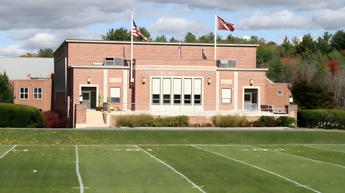 Das Backsteingebäude der The Governor's Academy mit großen Fenstern und amerikanischer Flagge im Hintergrund hinter einem Spielfeld.