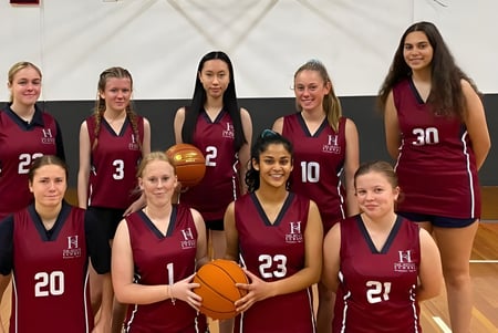 Eine Gruppe junger Schülerinnen in burgunderfarbenen Uniformen posiert mit Basketbällen auf dem Basketballplatz der The Heights School.