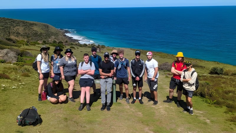 Eine Gruppe von Schülern der The Heights School steht auf einer grünen Anhöhe mit Blick auf das blaue Meer und die felsige Küste.