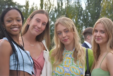 Vier Schülerinnen der The High School posieren gemeinsam lächelnd im Freien vor Bäumen und Grünflächen.