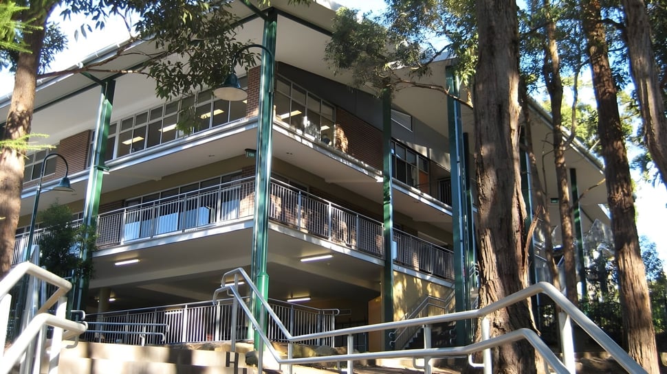 Das mehrstöckige Gebäude der The Hills Grammar School mit Balkonen ist von hohen Bäumen umgeben.