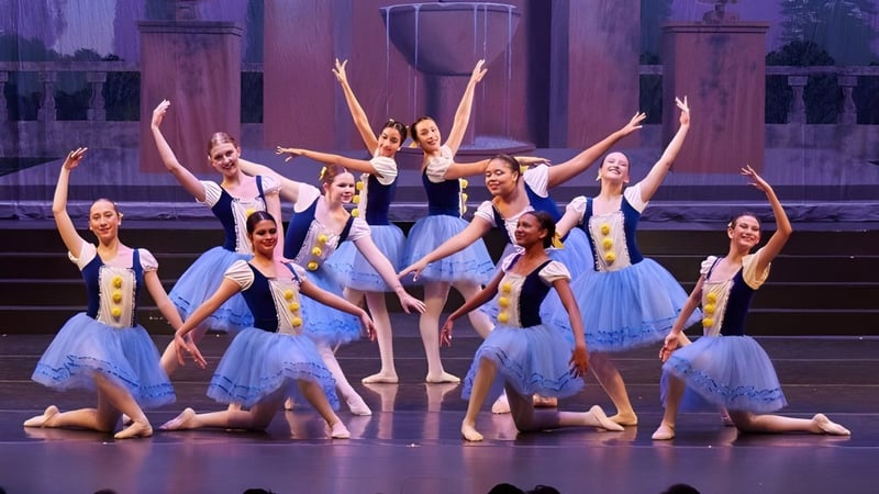 Eine Gruppe von Tänzerinnen führt auf der Bühne der The Hockaday School in bunten Kostümen vor farbig beleuchtetem Hintergrund auf.