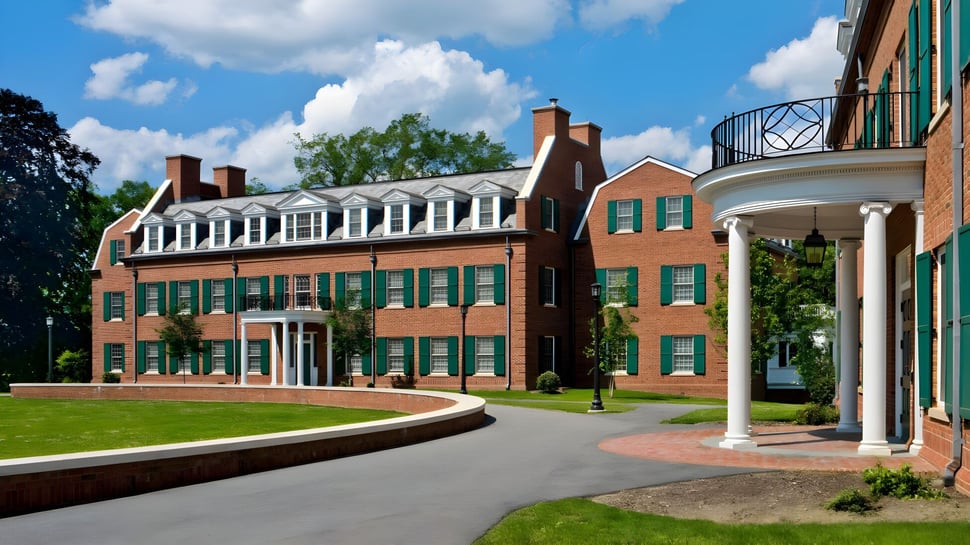 Das Backsteingebäude mit Säulenportikus auf dem Campus der The Hotchkiss School steht auf einem gepflegten Rasen unter blauem Himmel.