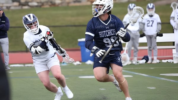 Zwei Lacrosse-Spieler der The Hotchkiss School laufen auf dem Sportplatz während weiterer Spieler im Hintergrund sichtbar sind.