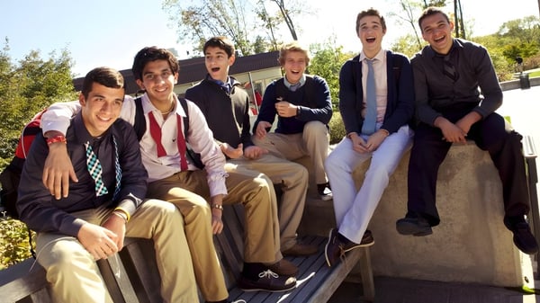 Eine Gruppe junger Männer in formeller Kleidung sitzt auf einer Steinmauer auf dem Campus der The Hun School of Princeton.