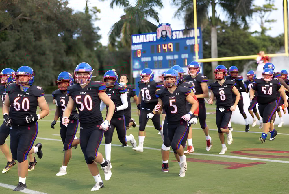 Eine Gruppe von Fußballspielern der The King's Academy läuft gemeinsam über das Spielfeld mit Palmen und Anzeigetafel im Hintergrund.