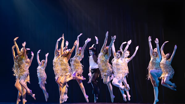 Eine Gruppe von Schülerinnen und Schülern der The King's Academy führt eine Tanzperformance in schimmernden Kostümen auf einer dunklen Bühne auf.