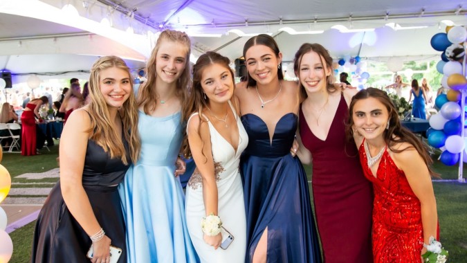 Eine Gruppe junger Frauen in formeller Kleidung posiert vor einem festlichen Hintergrund mit bunten Luftballons auf dem Campus von The Kings Hospital.