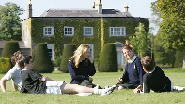 Eine Gruppe von Schülern sitzt auf dem Gras vor dem historischen Gebäude mit Turm auf dem Campus der The Kings Hospital.