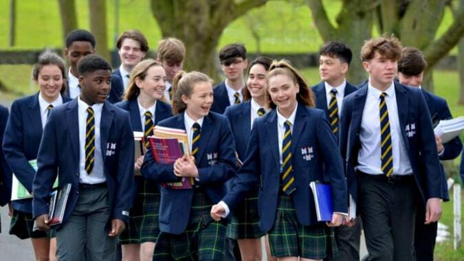 Eine Gruppe Schüler in Schuluniformen geht gemeinsam auf einem von grüner Vegetation umgebenen Weg auf dem Campus der The Kings Hospital.