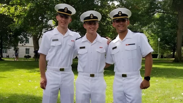 Drei Personen in weißen Marineuniformen stehen auf einem Rasen mit Bäumen im Hintergrund auf dem Gelände der The Kiski School.