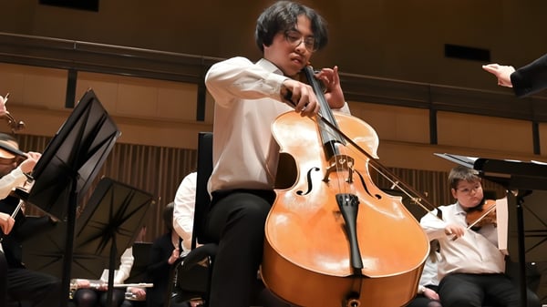Ein Mann spielt Cello auf der Bühne bei einem Konzert der The Leys School mit weiteren Musikern.