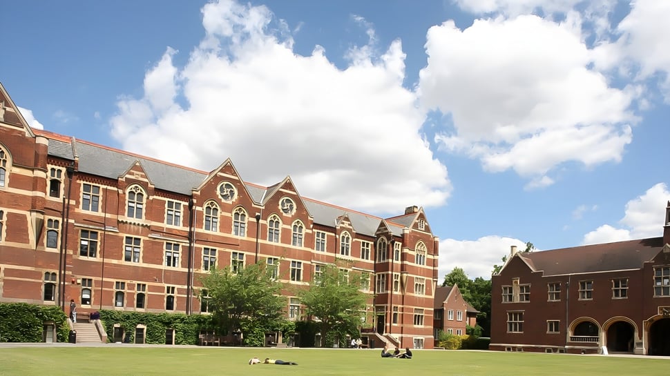 Das historische Backsteingebäude der The Leys School steht in einem grünen Innenhof mit Bäumen und blauem Himmel.