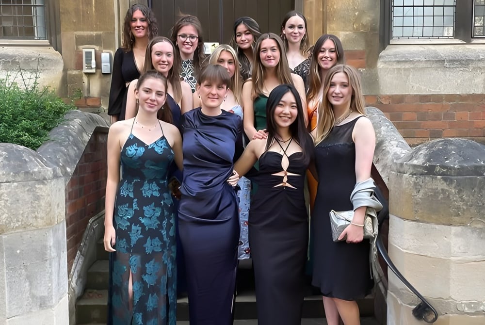 Eine Gruppe junger Frauen in formeller Kleidung steht gemeinsam vor einem historischen Steingebäude auf dem Campus der The Leys School.