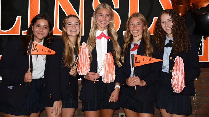 Eine Gruppe von Schülerinnen der The Linsly School steht in schwarzen Uniformen mit pinken Akzenten vor einem großen Lindy-Schild und hält pinke Pompons.