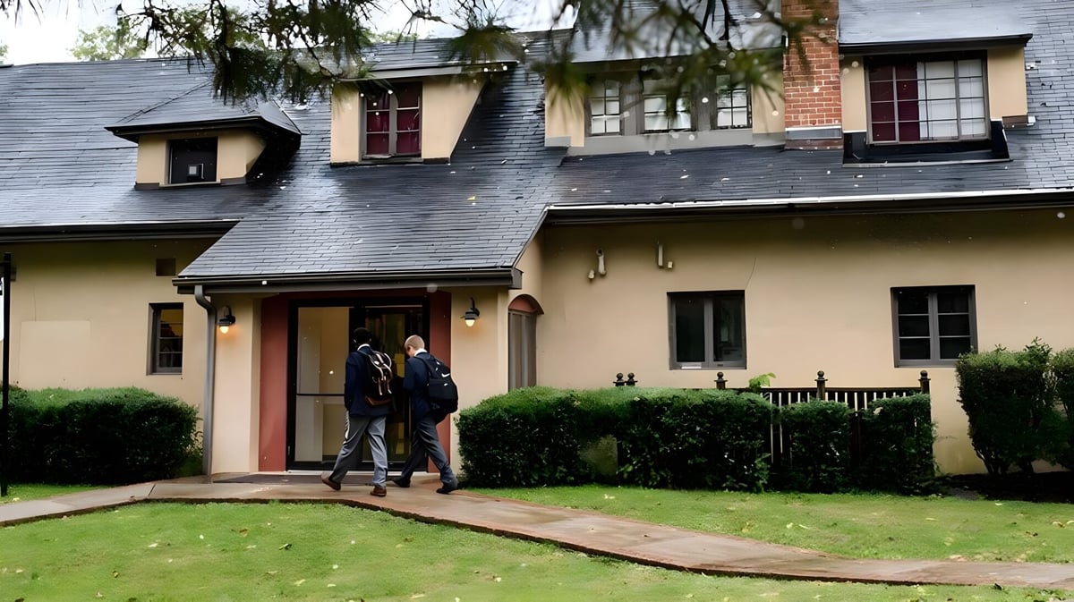 Das zweistöckige Backsteingebäude mit Veranda auf dem Campus der The Linsly School mit zwei Personen am Eingang.