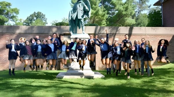 Eine Gruppe Schülerinnen und Schüler der The Linsly School steht vor einem Denkmal auf dem Campus mit Bäumen und Gebäuden im Hintergrund.
