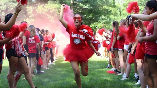 Eine Gruppe von Schülerinnen und Schülern in roten Kostümen hält Fahnen auf dem Outdoor-Gelände der The Madeira School.
