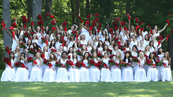 Eine Gruppe weiblicher Schülerinnen der The Madeira School steht im Wald und hält rote Rosen.
