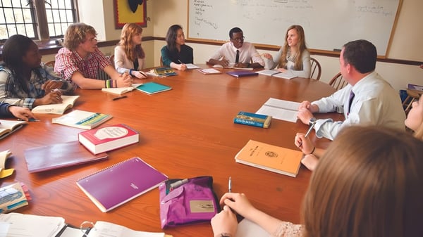 Eine Gruppe Schüler und eine Lehrkraft der The Masters School arbeiten gemeinsam an einem großen Holztisch im Klassenzimmer.
