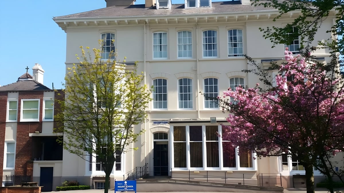 Das mehrstöckige Gebäude der The Mount School York ist von blühenden Bäumen und klarem Himmel umgeben.