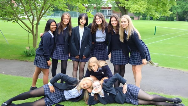 Eine Gruppe Schülerinnen der The Mount School York steht auf einer Wiese vor Bäumen.