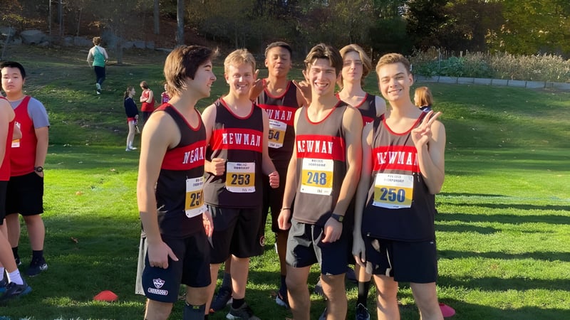 Eine Gruppe junger Athleten steht auf dem Sportfeld der The Newman School mit Bäumen und weiteren Läufern im Hintergrund.