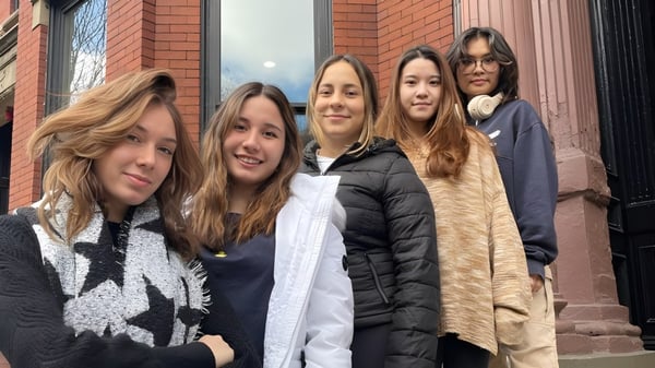 Eine Gruppe junger Frauen steht vor einem Backsteingebäude auf dem Campus der The Newman School und unterhält sich.
