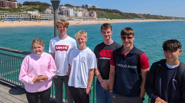 Schüler der The Oratory School stehen auf einem Steg und blicken auf eine Küstenstadt mit bunten Gebäuden und blauem Meer.