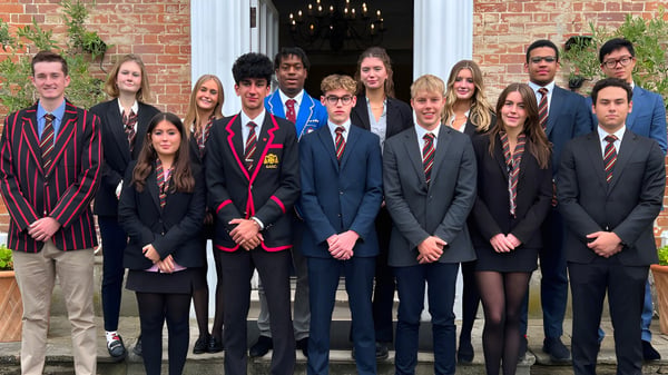 Eine Gruppe Schüler der The Oratory School steht in formeller Kleidung vor einem Backsteingebäude mit einem Kronleuchter im Eingang.