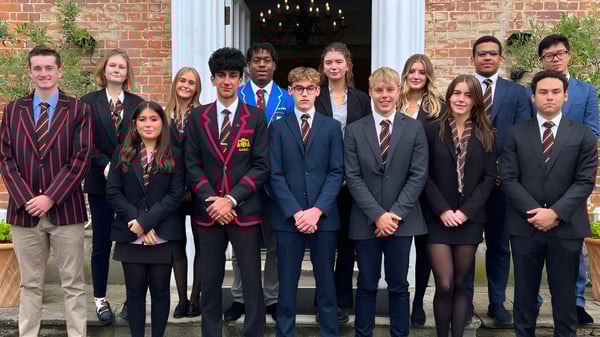 Eine Gruppe Schüler der The Oratory School steht in formeller Kleidung vor einem Backsteingebäude mit einem Kronleuchter im Eingang.