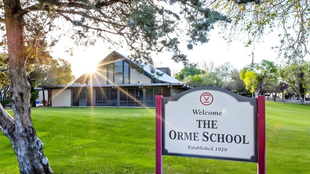 Das moderne Schulgebäude der The Orme School steht im grünen Gras mit Bäumen und Sonnenschein im Hintergrund.