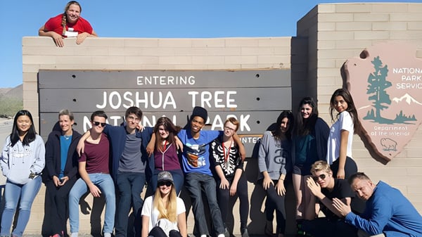Schülerinnen und Schüler der The Orme School stehen vor dem Eingangsschild des Joshua Tree National Parks in der Wüstenlandschaft.