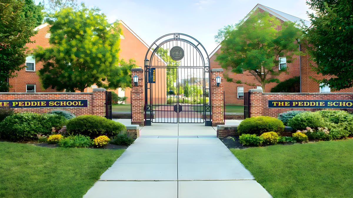 Der Eingang zur The Peddie School mit einem gemauerten Torbogen und Blick auf den gepflegten Campus mit Grünflächen und Gebäuden.