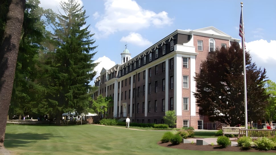Das große Backsteingebäude mit Turm auf dem Campus der The Pennington School ist von Rasen und Bäumen umgeben.