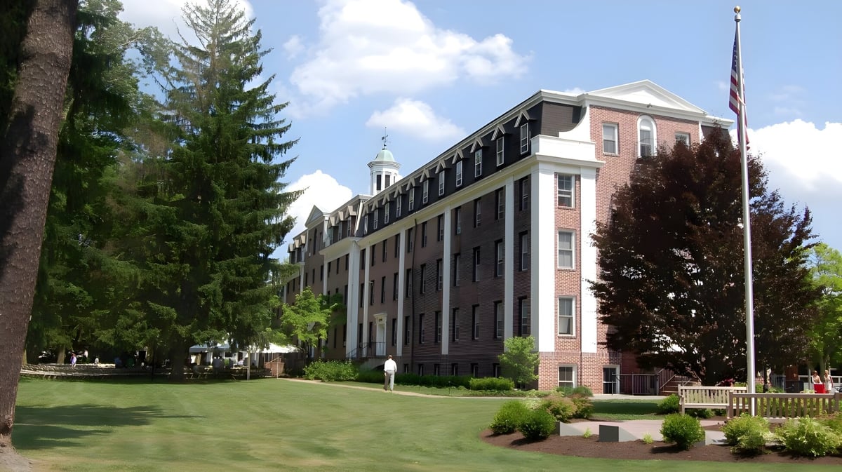 Das große Backsteingebäude mit Turm auf dem Campus der The Pennington School ist von Rasen und Bäumen umgeben.
