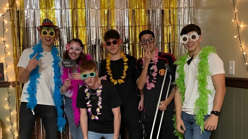 Eine Gruppe Schüler der The Phelps School posiert vor einem Hintergrund aus goldenen und silbernen Vorhängen in bunten festlichen Outfits.