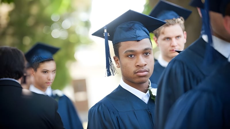 Eine Gruppe von Absolventinnen und Absolventen der The Phelps School steht in schwarzen Talaren unter freiem Himmel vor Bäumen.
