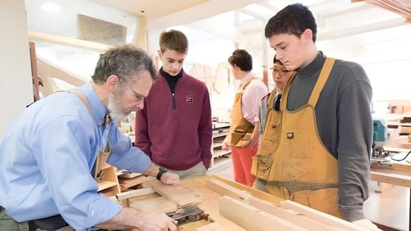 Eine Gruppe von Schülern und ein älterer Mann arbeiten gemeinsam an einem Arbeitstisch auf dem Campus der The Salisbury School.