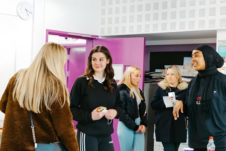 Eine Gruppe Schülerinnen der The Sheffield College steht in einem Flur mit rosa Wand im Hintergrund.