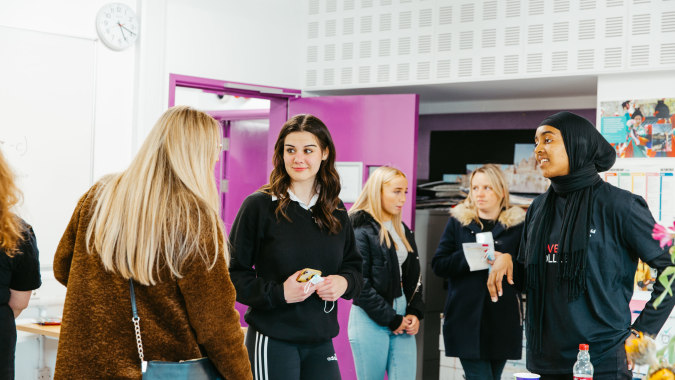 Eine Gruppe von Schülerinnen und Schülern steht im Flur des The Sheffield College vor einer weißen und pinkfarbenen Wand.