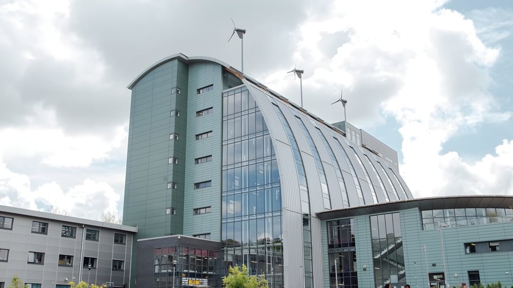 Das moderne Glas- und Stahlgebäude des The Sheffield College mit geschwungener Fassade unter bewölktem Himmel.