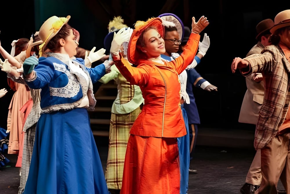 Eine Gruppe von Tänzern in bunten Kostümen führt eine Darbietung auf der Bühne der The Stony Brook School auf.