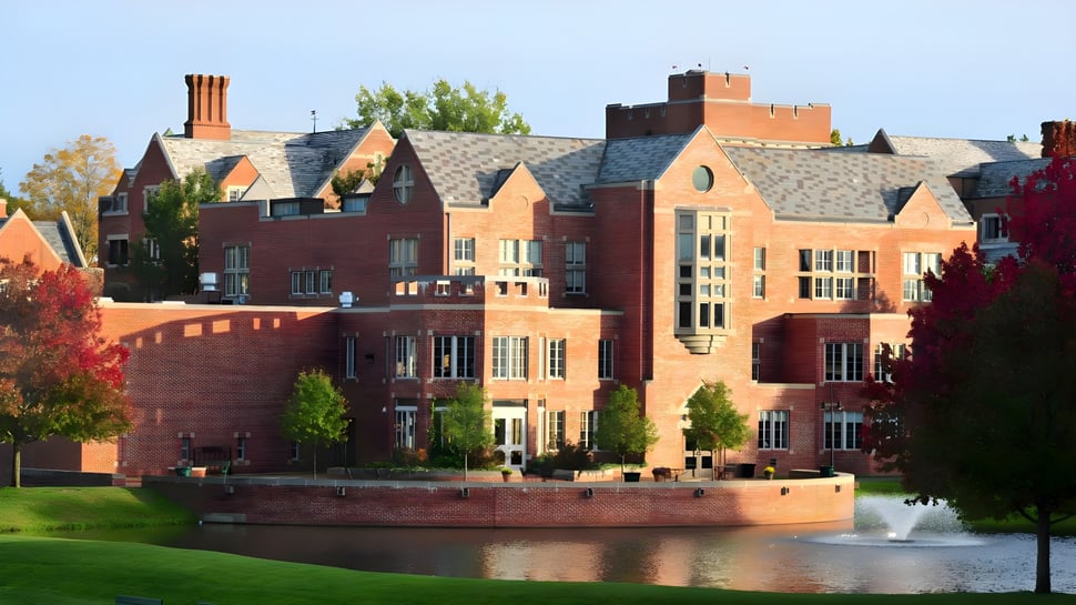 Das Backsteingebäude der Taft School mit einem Teich und Springbrunnen im Vordergrund unter blauem Himmel.
