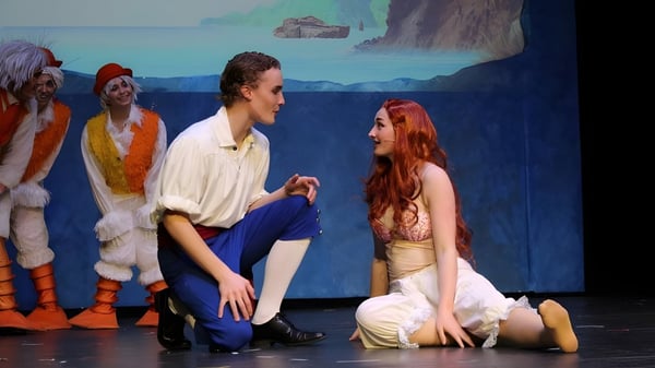 Eine Theateraufführung zeigt ein Paar auf der Bühne vor einer Kulisse mit Ozeanlandschaft auf dem Campus der The Vanguard School.